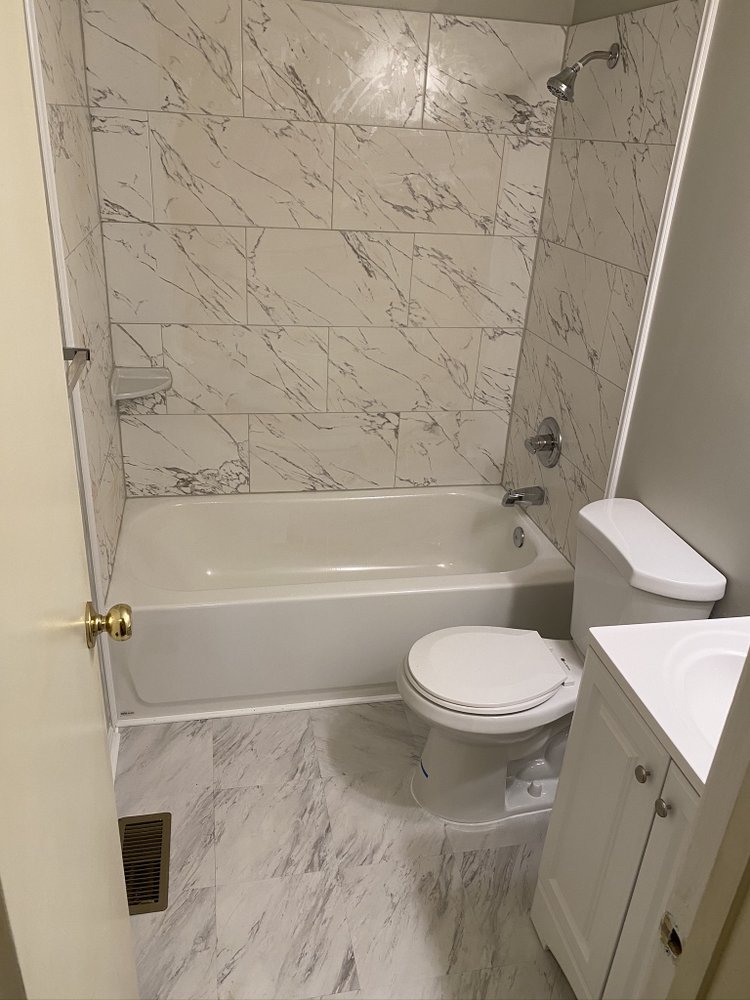 Finished bathroom with a white tub set into a marble-patterned tiled surround running full height, tiled floor and toilet.