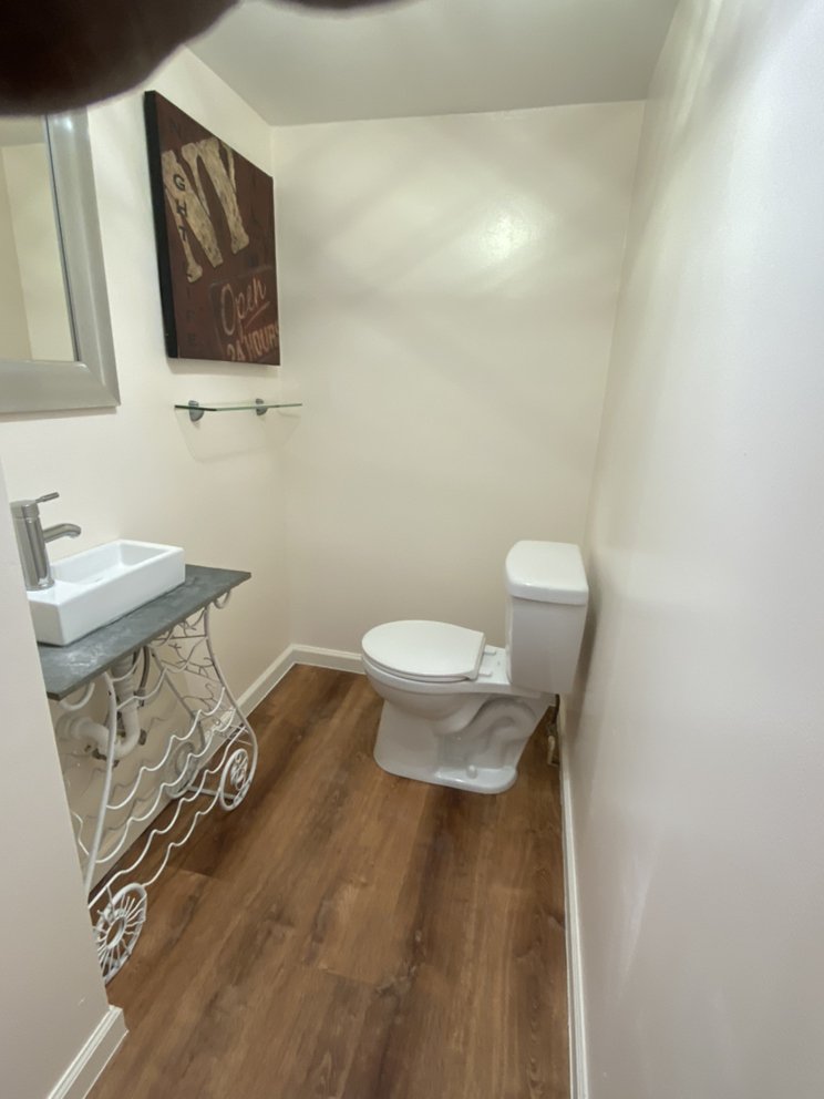 Small finished powder room with a square vessel basin on a dark top, toilet and wood-effect plank flooring.