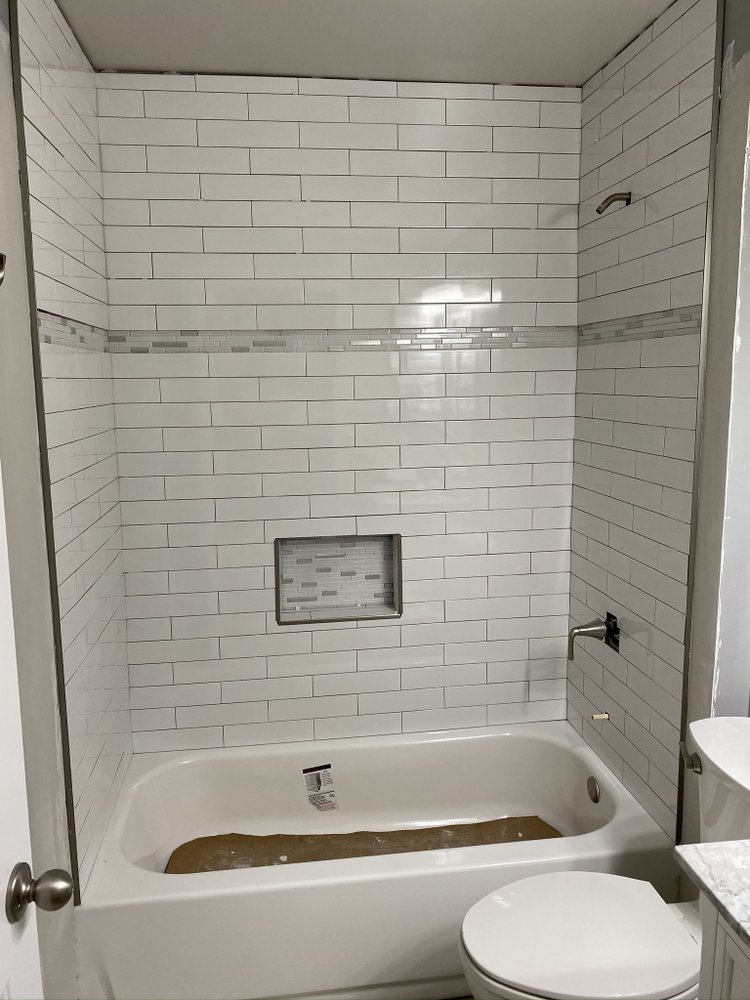 Finished tub and shower in white subway tile with a mosaic accent band and a recessed shampoo niche.