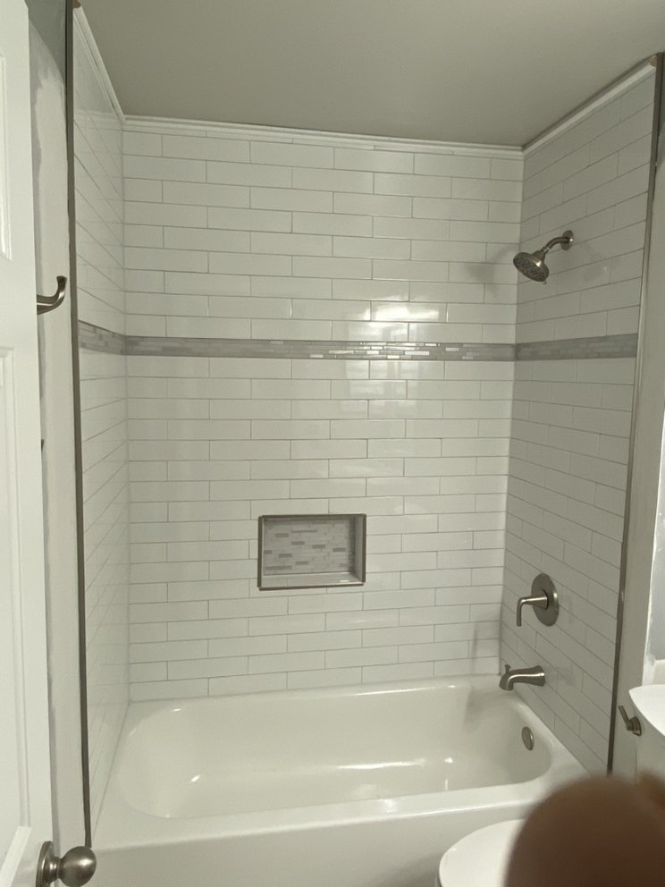 Finished tub with a white tiled surround, a horizontal mosaic accent band and a recessed niche.