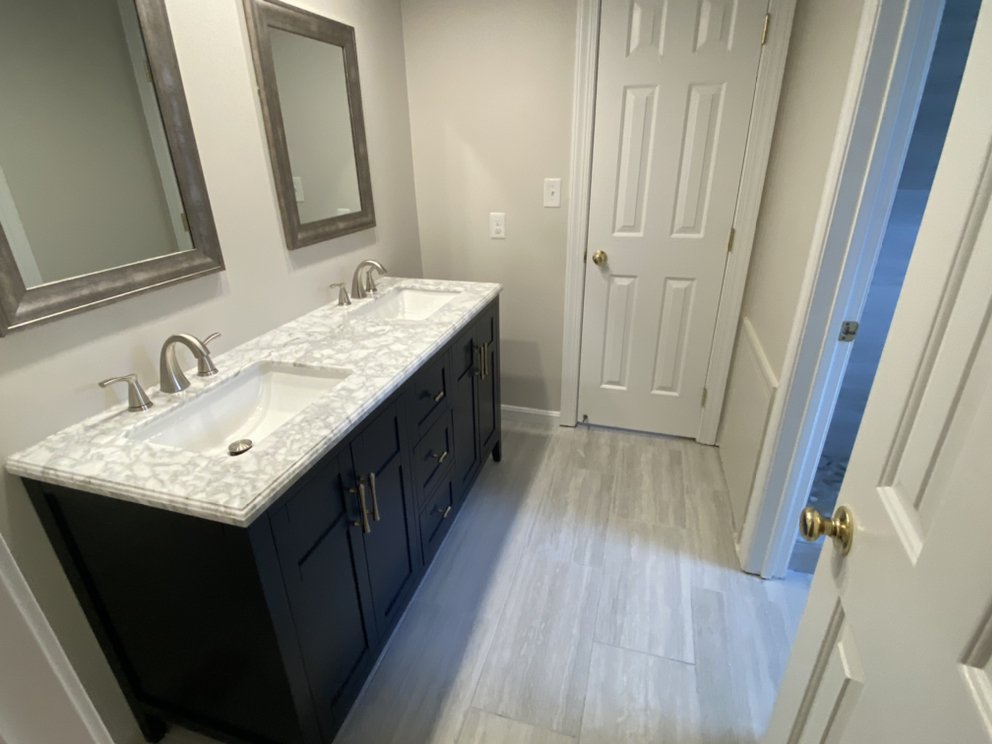 Finished bathroom with a navy vanity, marble-effect countertop, framed mirror and pale plank flooring.