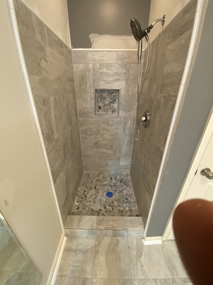 Finished walk-in shower lined in large stone-effect tile with a pebble mosaic floor and a recessed niche.
