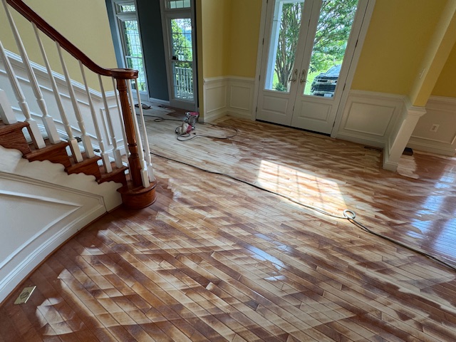 Living room with a newly refinished hardwood floor beside a staircase and tall windows.