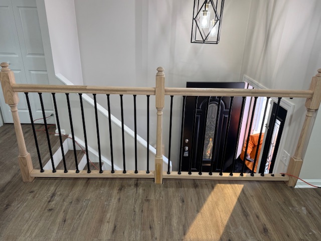Completed upstairs guardrail with timber posts and black balusters around a stair opening.