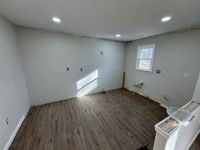 Empty room with newly installed brown plank flooring, grey walls and recessed lights.