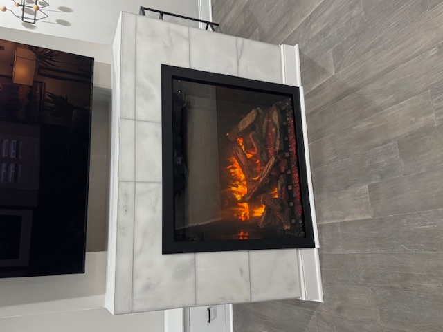 Finished black fireplace inset into a large-format pale tiled feature wall.