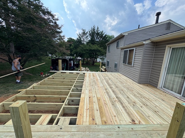 Backyard deck under construction with exposed joists and boards being installed from the house outward.