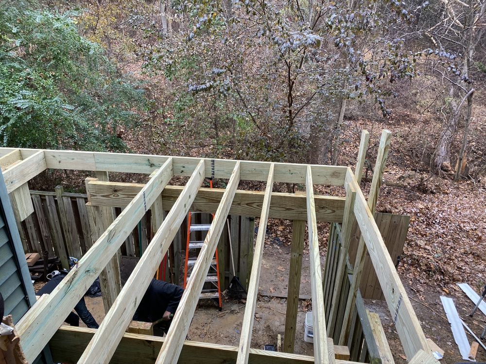 New pressure-treated deck framing built out over a sloping wooded yard, posts and beams in place before boards go down.