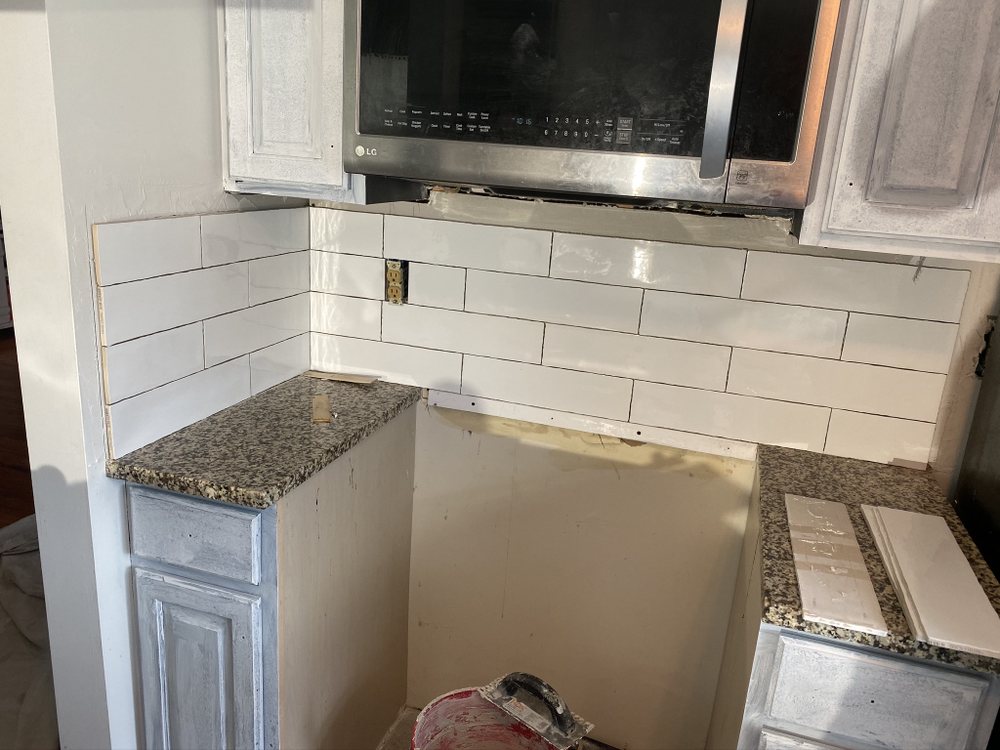 Close view of a white tiled kitchen backsplash meeting granite counter and upper cabinets.