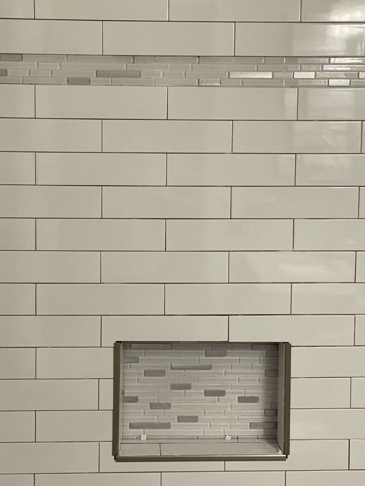 Close view of a recessed shower niche lined in mosaic tile, set into a wall of white subway tile.